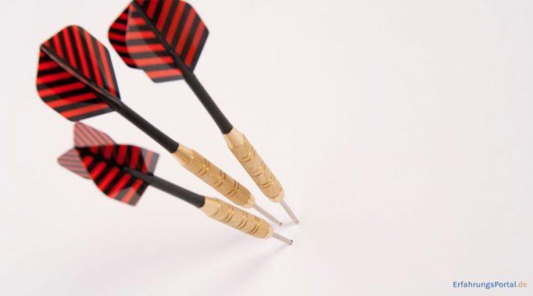 Drei Dartpfeile stecken entweder in einer weißen Wand oder in einem weißen Papier