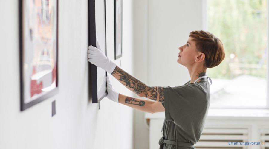 Eine Frau richtet ein Kunstwerk im Rahmen mit weißen Handschuhen aus