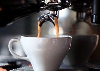 Eine Tasse steht unter einer Kaffeemaschine und der frische Kaffee fließt in die Tasse