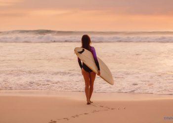 Eine Frau mit Surfbrett steht am Meer