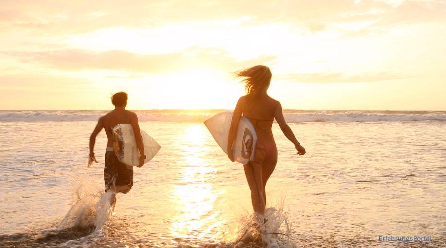 zwei Surfer laufen beim Sonnenuntergang mit den Surfbrettern ins Meer