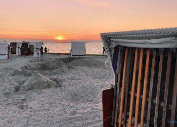 Strandkörbe am Strand. Im Hintergrund sieht man das Meer, den Sonnenuntergang und einige Personen