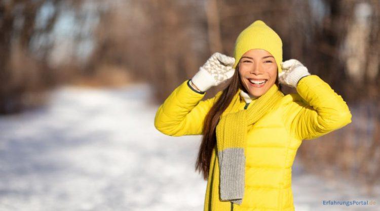 Frau im Schnee mit hellgelber Jacke, Schal und Mütze