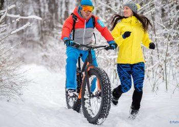 Mann fährt im Schnee Fahrrad während eine Frau nebenher joggt