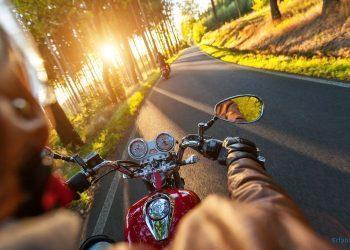 Motorradfahrer fährt bei Sonnenuntergang durch eine Allee