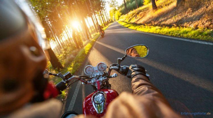 Motorradfahrer fährt bei Sonnenuntergang durch eine Allee