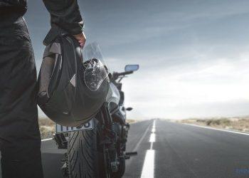 Motorradfahrer steht auf der Straße und hält seinen Motorradhelm in der rechten Hand. Vor ihm steht sein Motorrad