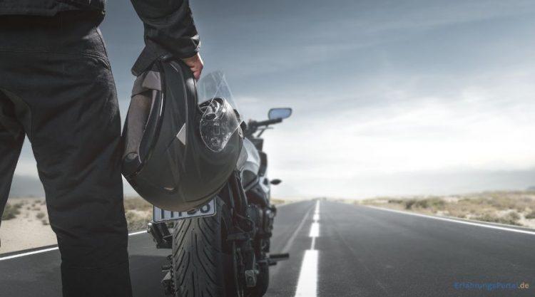 Motorradfahrer steht auf der Straße und hält seinen Motorradhelm in der rechten Hand. Vor ihm steht sein Motorrad