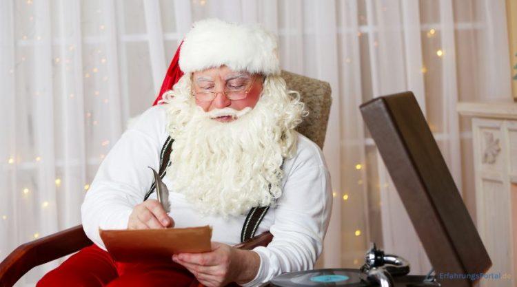Der Weihnachtsmann sitzt auf einem Sessel und liest einen Brief. Er hält eine Feder in der Hand. Neben ihm steht ein Plattenspieler