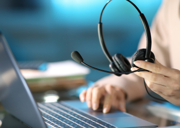 Jemand hält ein Headset in der Hand, während derjenige mit der anderen Hand etwas auf dem Laptop klickt