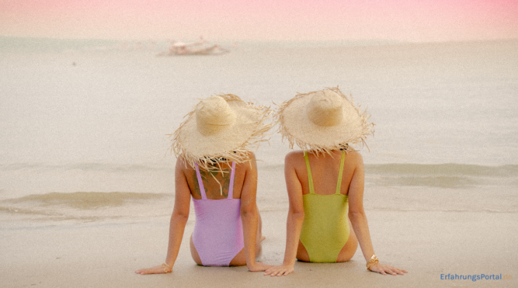 zwei Frauen in Badeanzug sitzen am Strand bei Sonnenuntergang